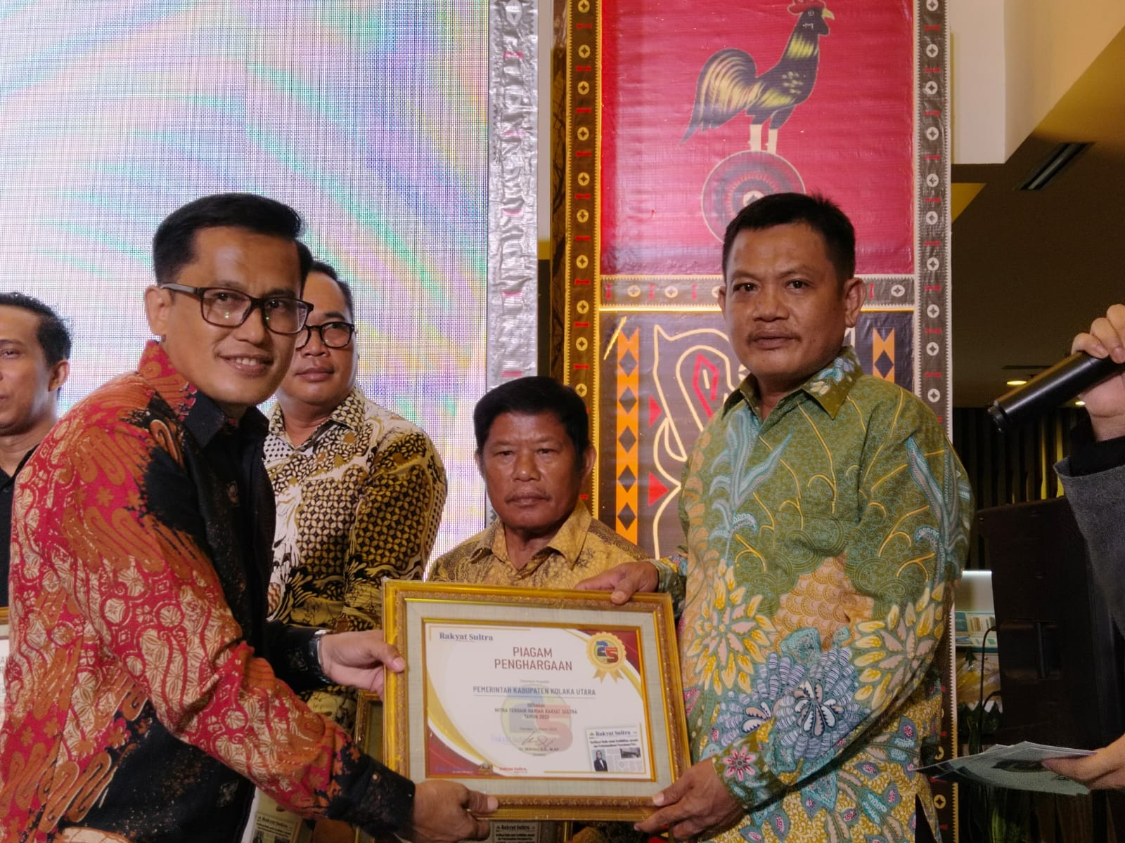 Dr. Mahdar, S.S., M.AP, selaku Direktur Harian Rakyat Sultra, menyerahkan langsung Piagam Penghargaan kepada Kadis Kominfo Kolaka Utara, Batman Batau, S.Pd., M.Pd.